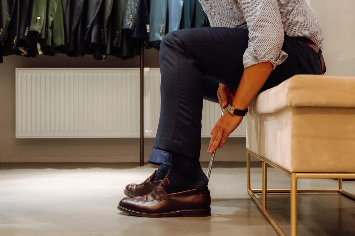 Sélection de cravates grise, noire et rose devant un portant de costumes bleus dans une boutique belge